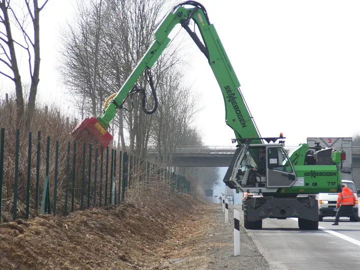 Forestry mulcher attachment on an excavator clearing roadside vegetation (stock photo)